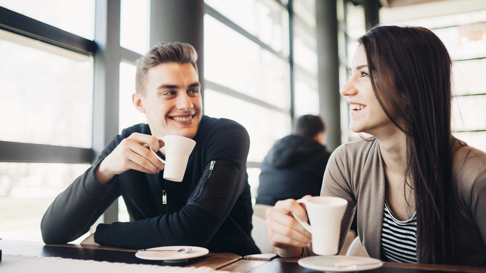 A heterosexual couple laughing over coffee at a cozy table