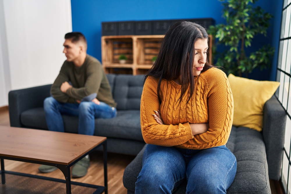 A heterosexual couple sitting apart on a couch, gazing in opposite directions-Caption: